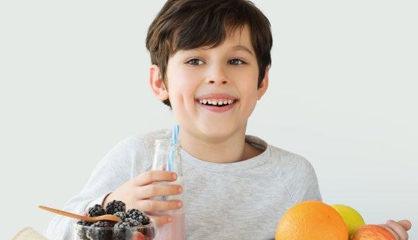 niño toma yogurt rodeado de alimentos con vitamina a como la naranja
