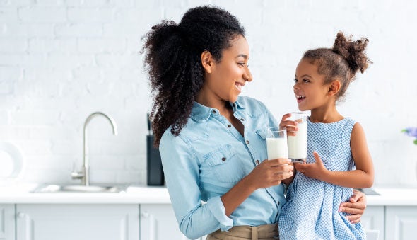 Una madre abraza a su hija sonriente que bebe leche
