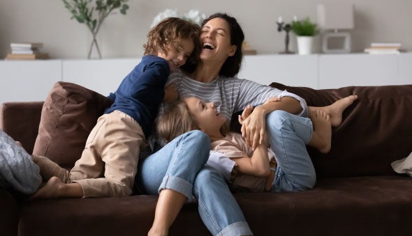 Una madre juega y ríe con sus hijos en el sofá de la sala
