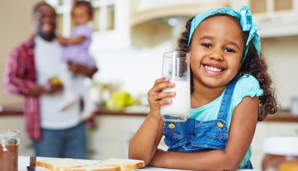 Niña tomando leche con su familia de fondo