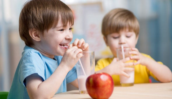  Niños tomando leche mientras hay una manzana en la mesa