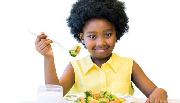 Niña comiendo de un plato con verduras junto a un vaso con leche