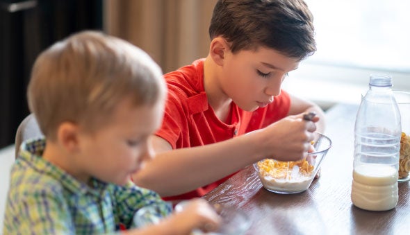 Dos niños comiendo cereal con alimento lácteo
