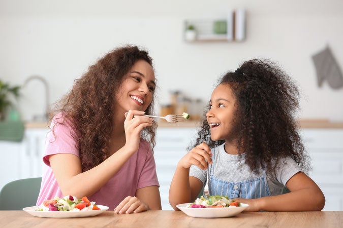 Mamá dándole comida a su hija mientras promueve una buena alimenteción