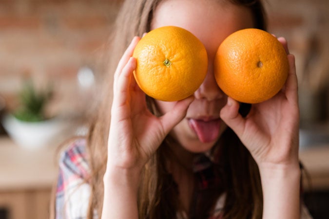 Niña sosteniendo dos naranjas simulando que son sus ojos